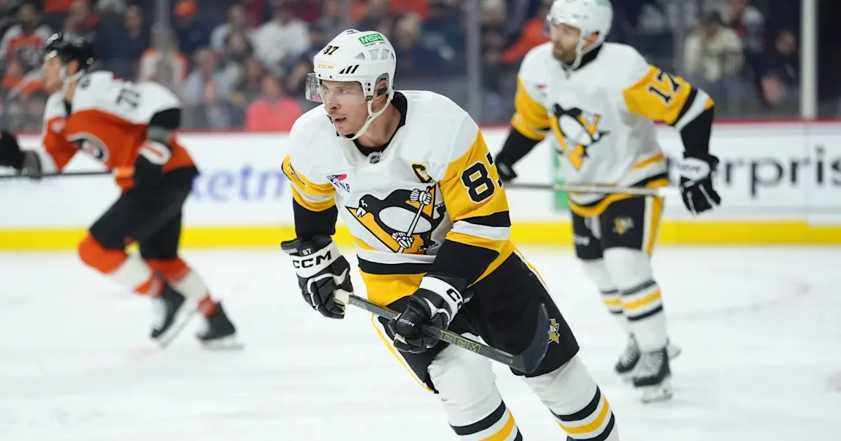 A Penguins player in a white and yellow uniform skates with the puck as Flyers and Penguins players follow.