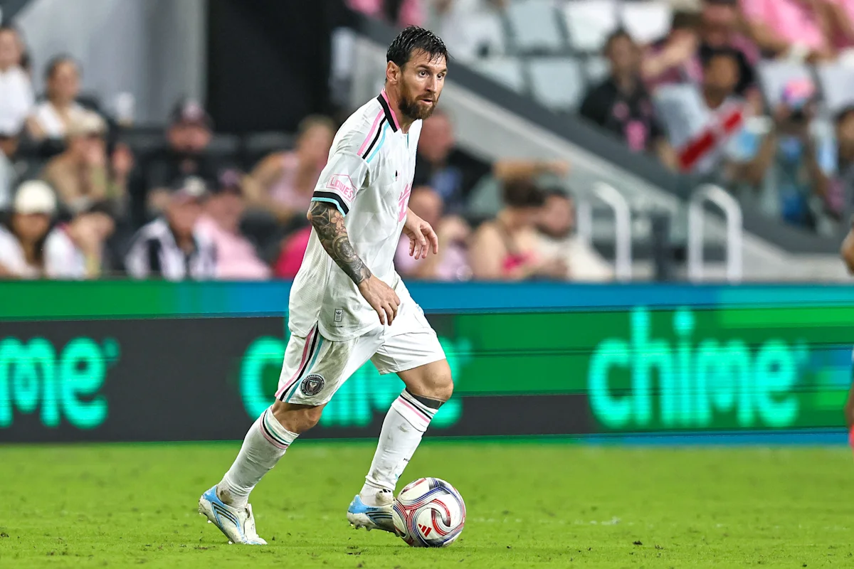 Soccer player in white kit dribbles the ball across a field during a match.