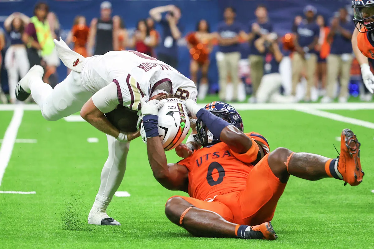 UTSA football player in orange tackles an opposing player in white on the field