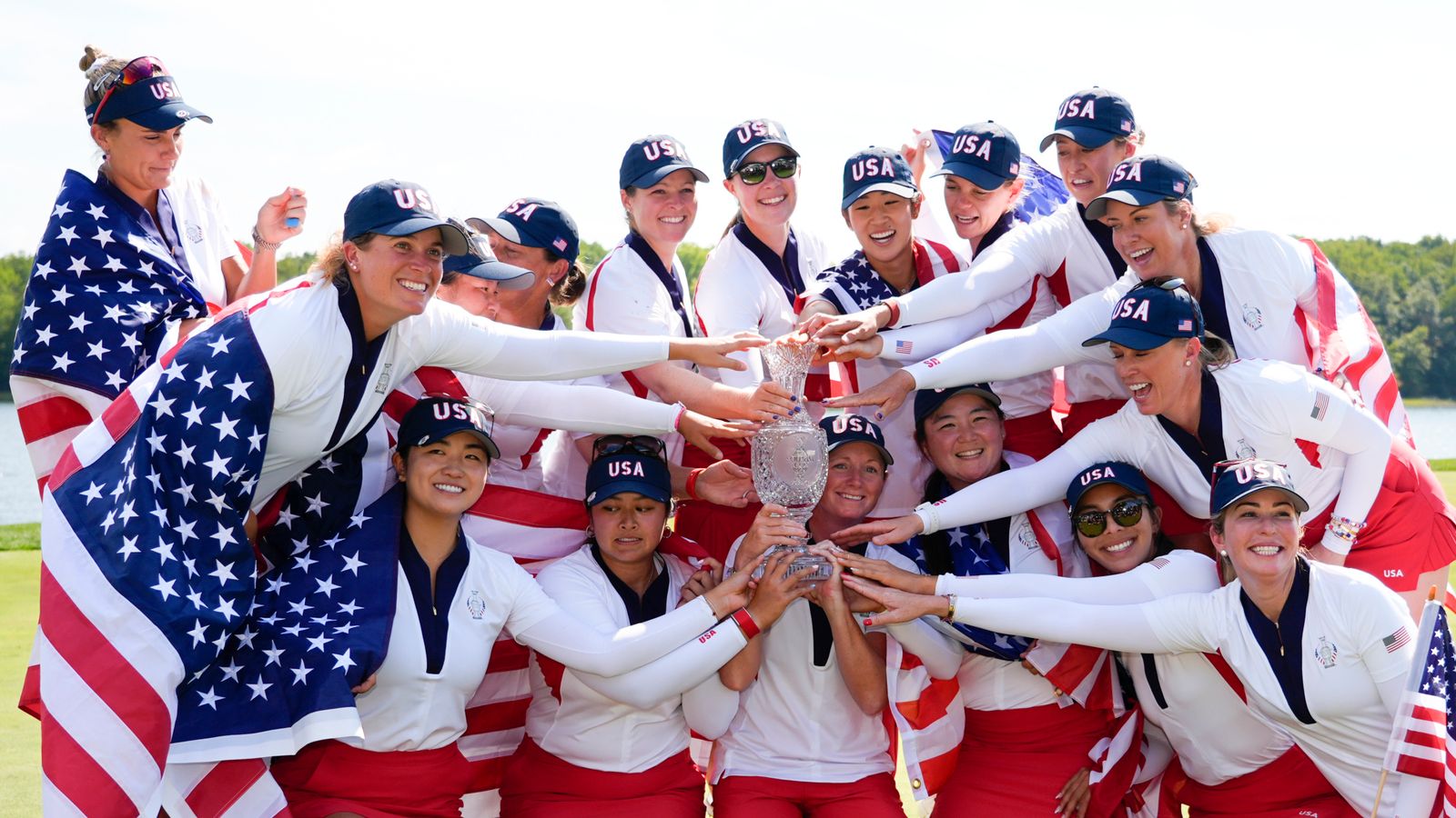 United States women's golfers gather around a trophy, smiling and celebrating in team uniforms.