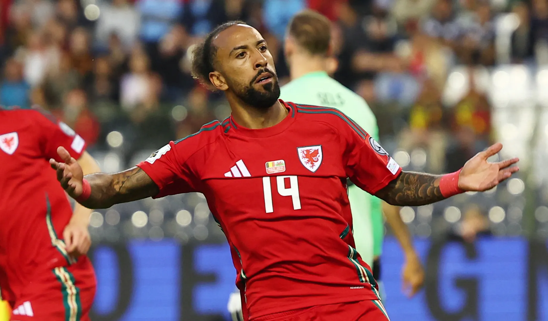 Wales footballer in red jersey number 19 celebrates with arms outstretched during a match.