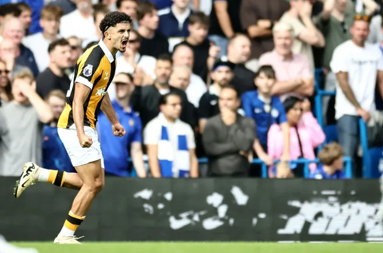 Footballer in black and gold kit celebrates during a match in front of spectators