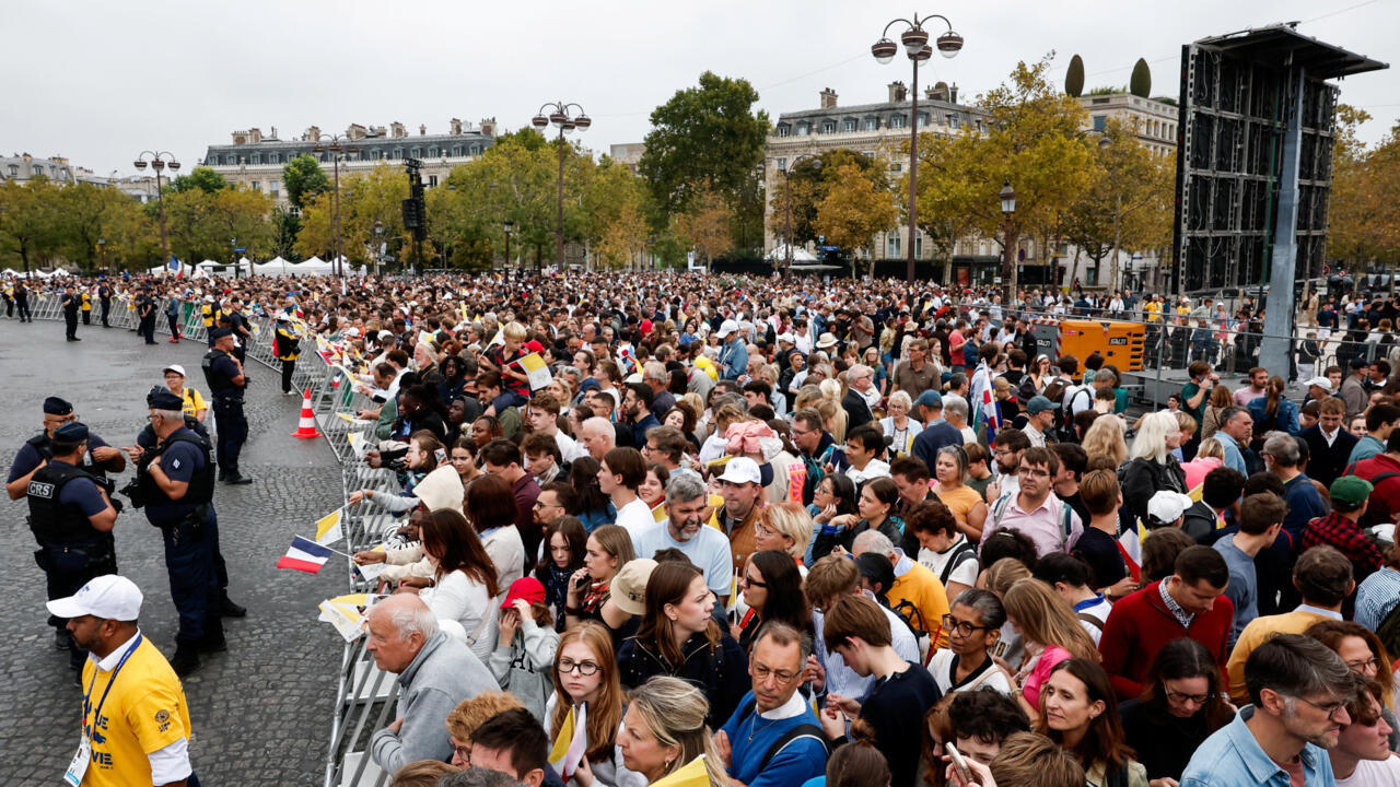 A dense crowd gathers behind barriers as police officers stand beside an event stage.
