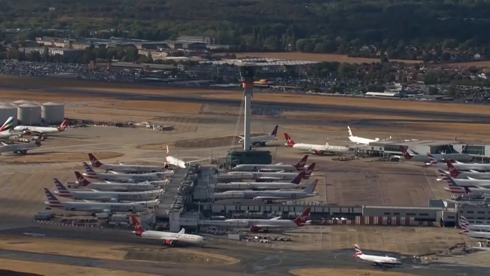 Aerial view of numerous passenger aircraft parked around airport terminals and taxiways.