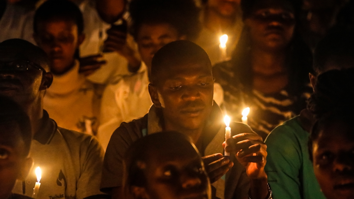People hold lit candles in a dimly lit gathering, their faces illuminated by candlelight.