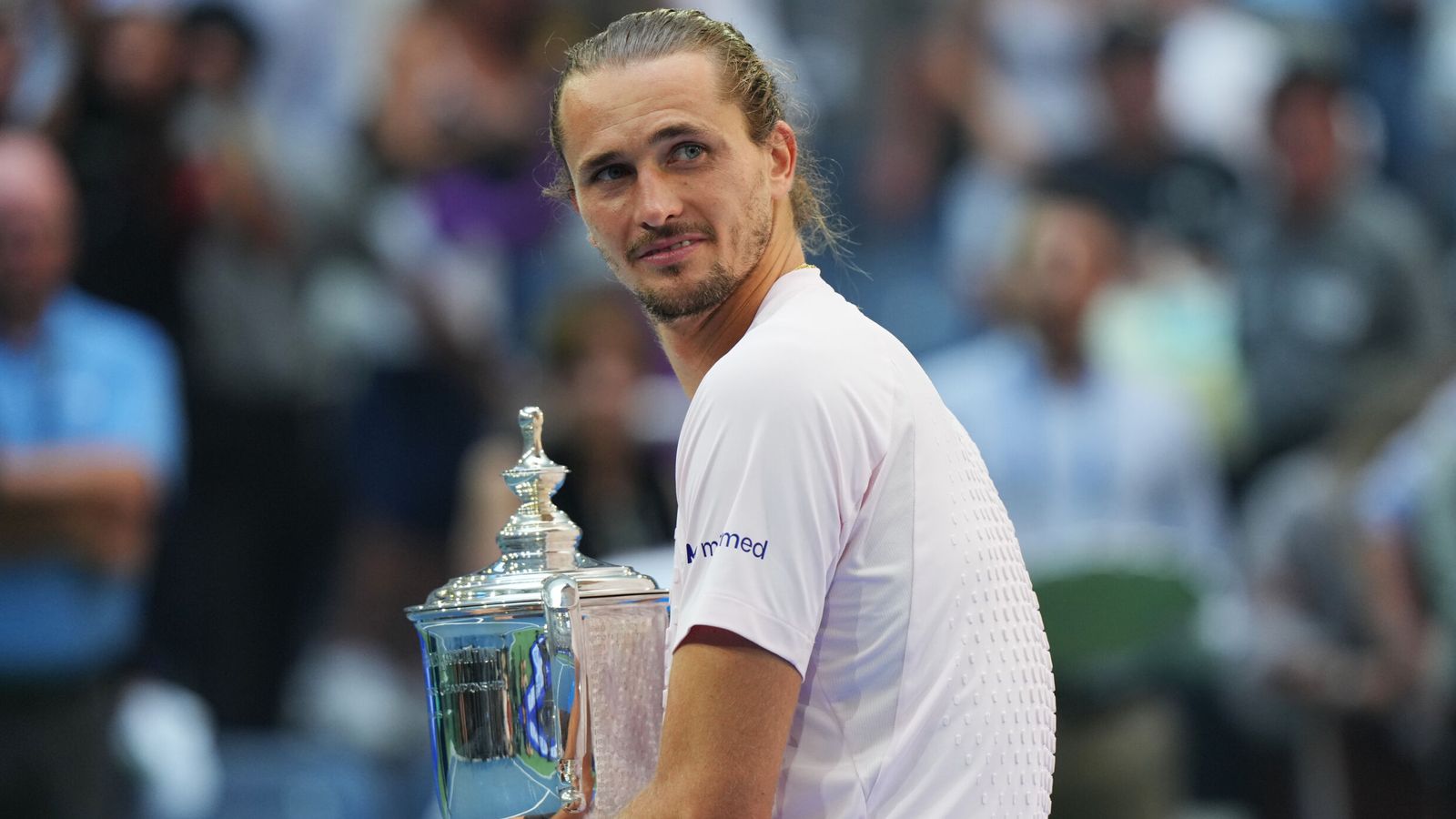 Tennis player holding a silver trophy and looking over his shoulder toward the camera