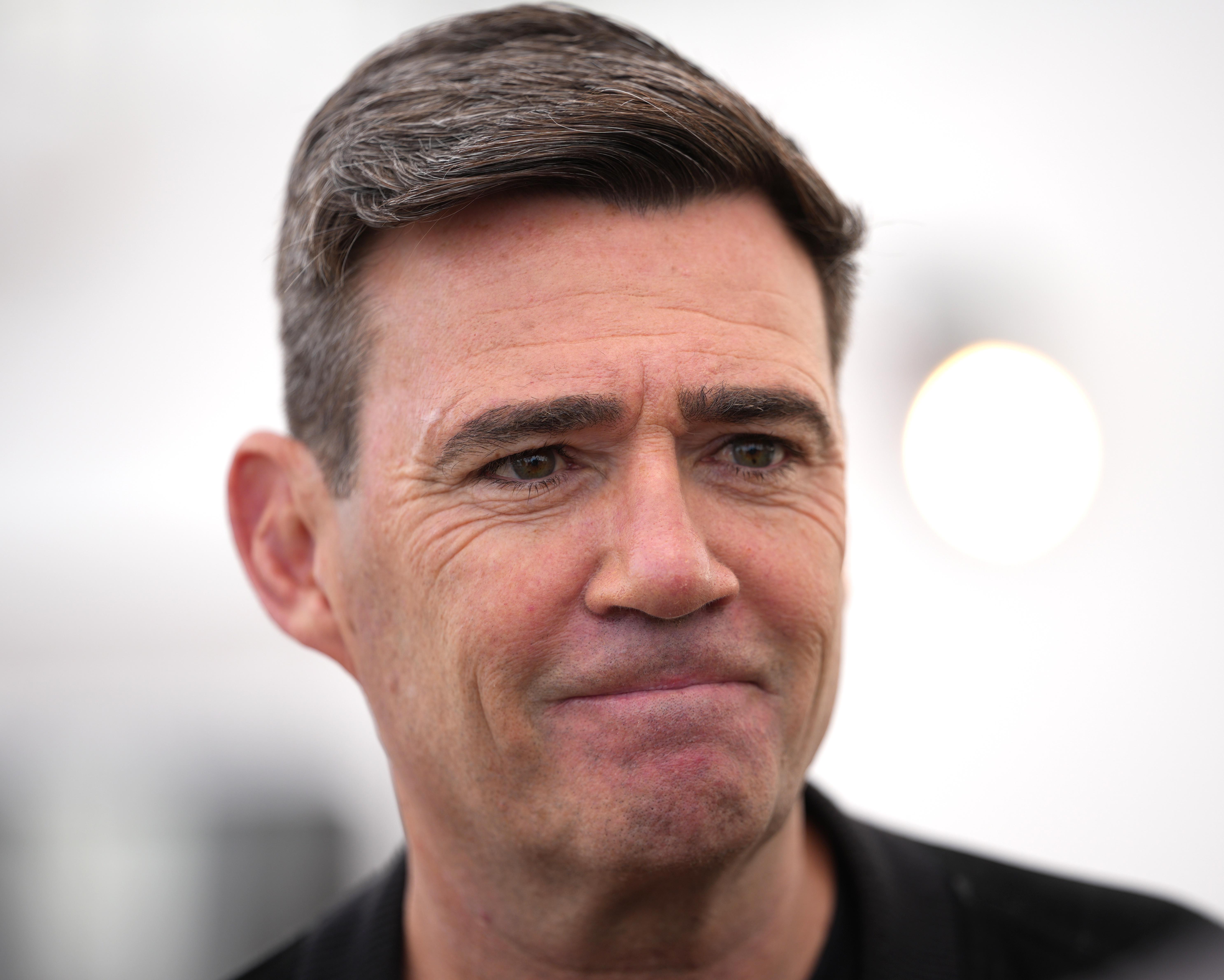 Close-up portrait of a dark-haired man in a black jacket against a bright, blurred background.