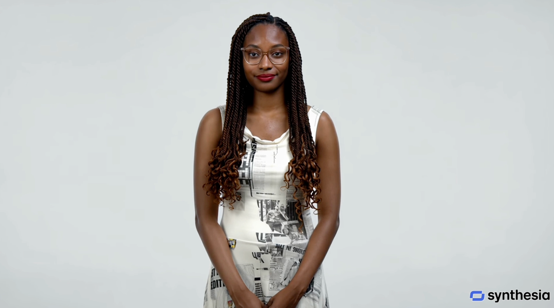 A woman with glasses and long braids stands against a pale background, wearing a printed white dress.