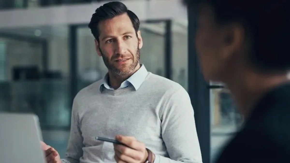 Man holding a tablet while speaking with another person in a modern office