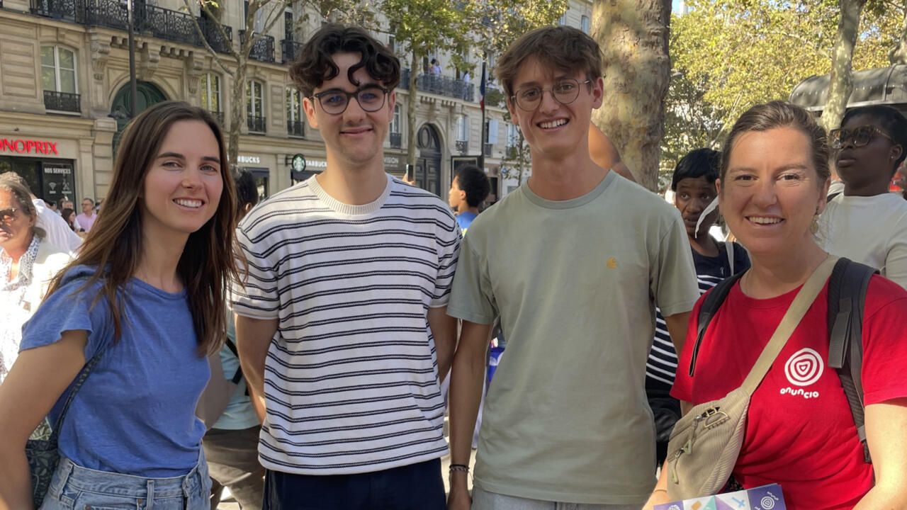 Four smiling people pose in a busy city street, with pedestrians and historic buildings behind them.