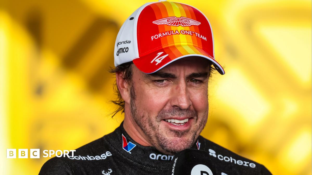 Fernando Alonso smiles in an Aston Martin cap and racing suit against a bright yellow background.