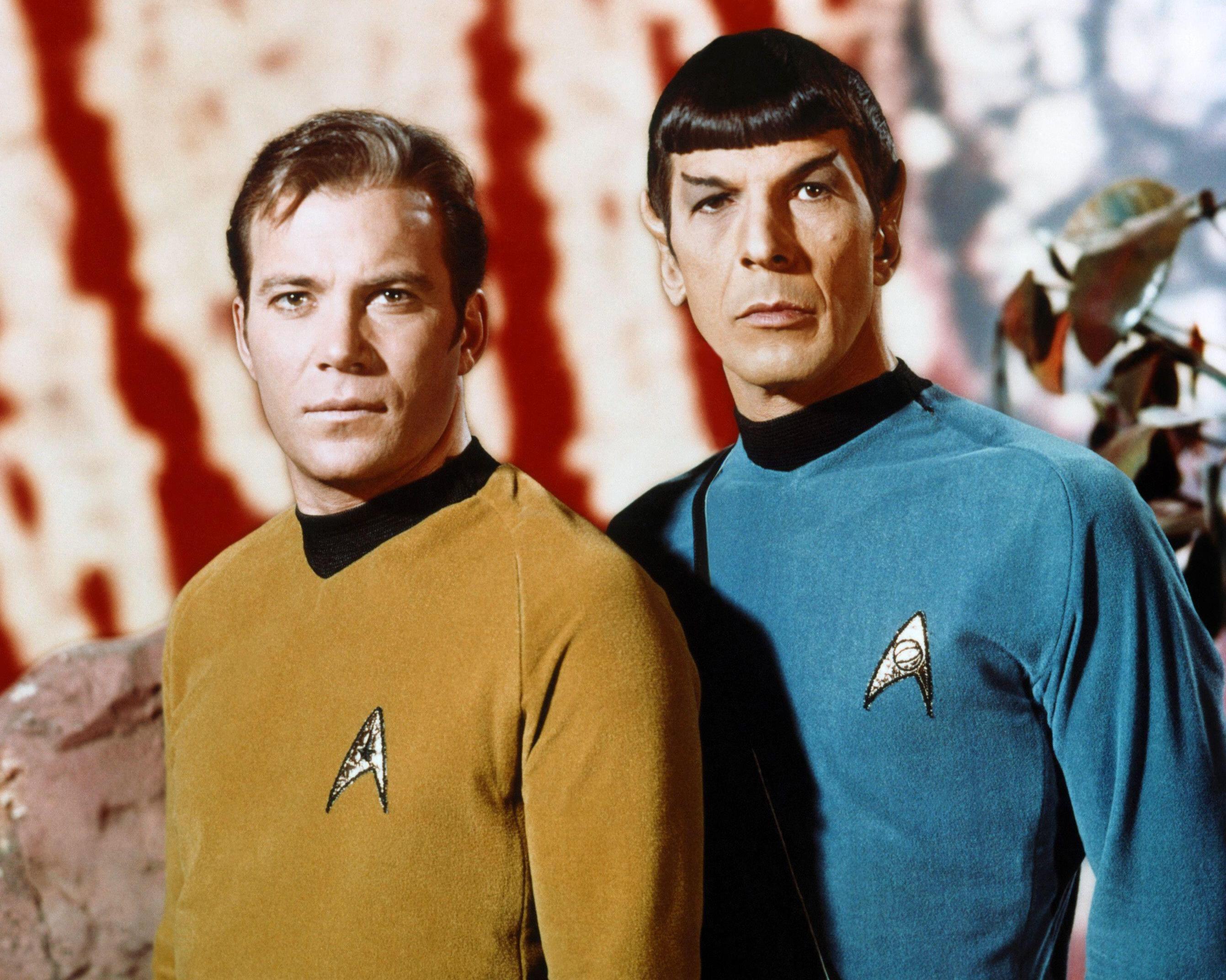 Two men in gold and blue Star Trek uniforms stand side by side indoors.