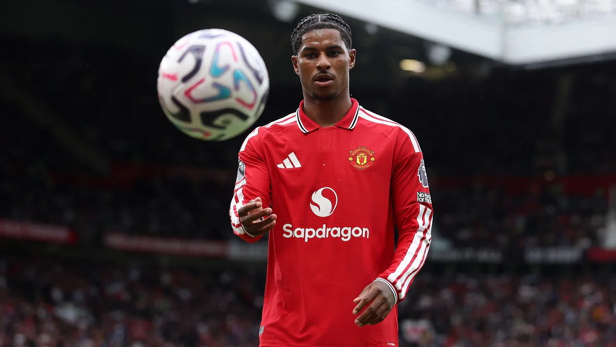 Footballer in red Manchester United jersey watches a ball floating nearby inside a stadium.