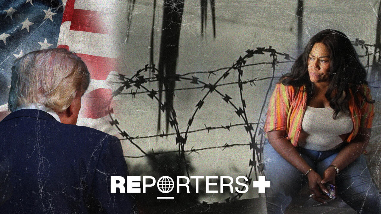 Seated woman faces a suited man beside barbed wire and a partially visible American flag.