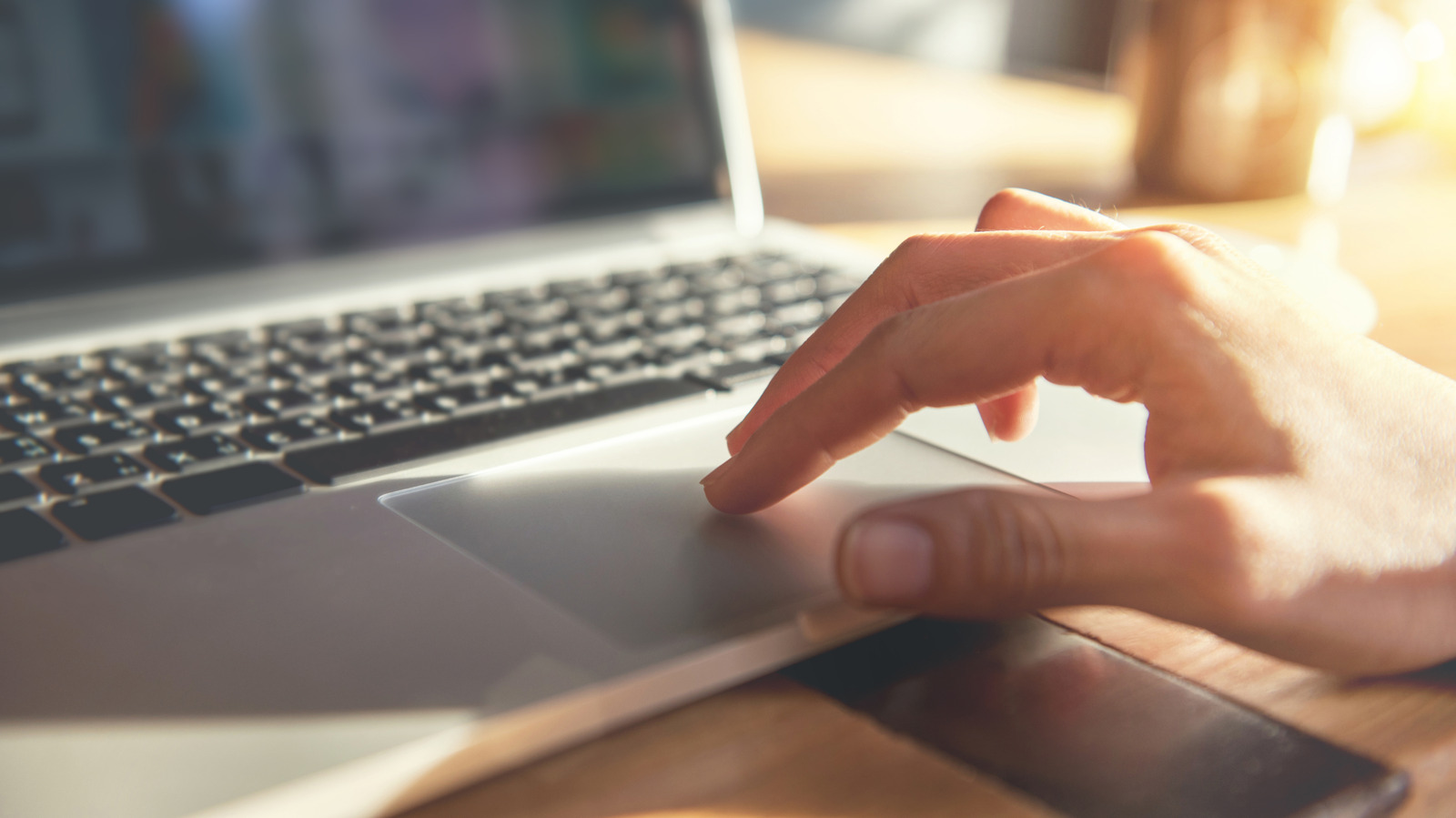 Hand using a laptop trackpad in warm sunlight beside the keyboard