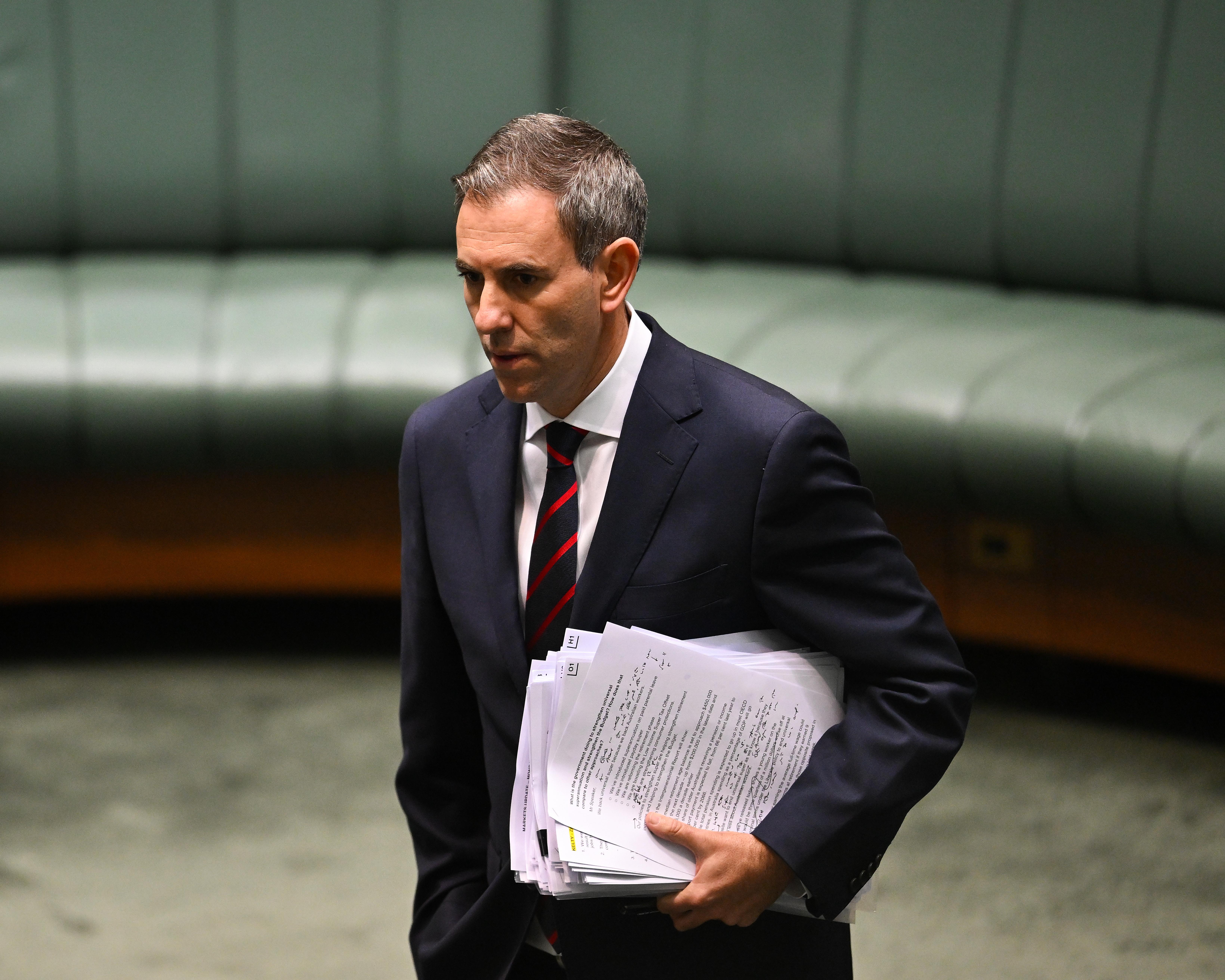 Suited man carrying a large stack of documents through an indoor chamber