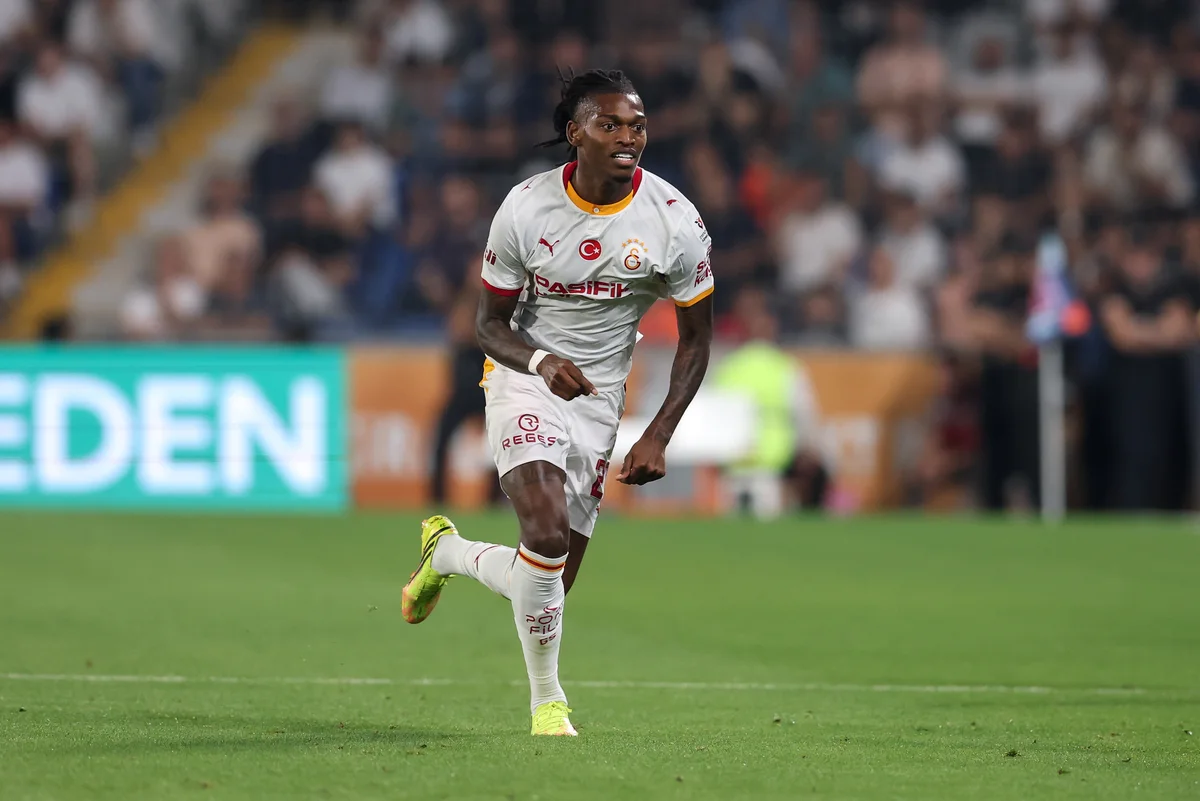 Footballer in white Galatasaray kit runs across the pitch during a match.