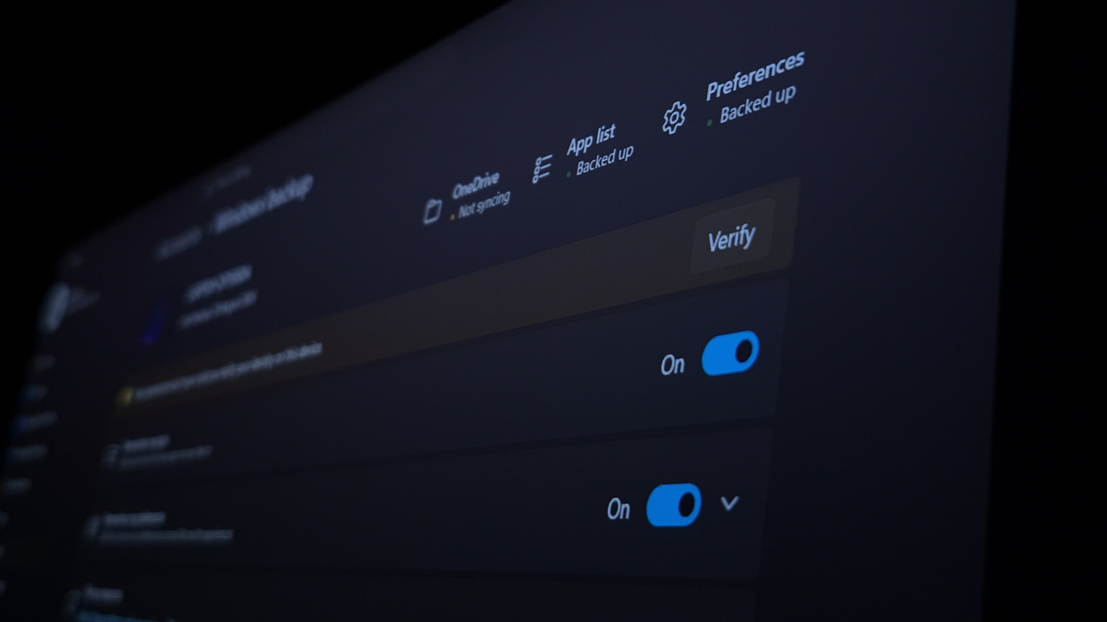 Angled close-up of a Windows settings screen with blue toggles and backup status labels.