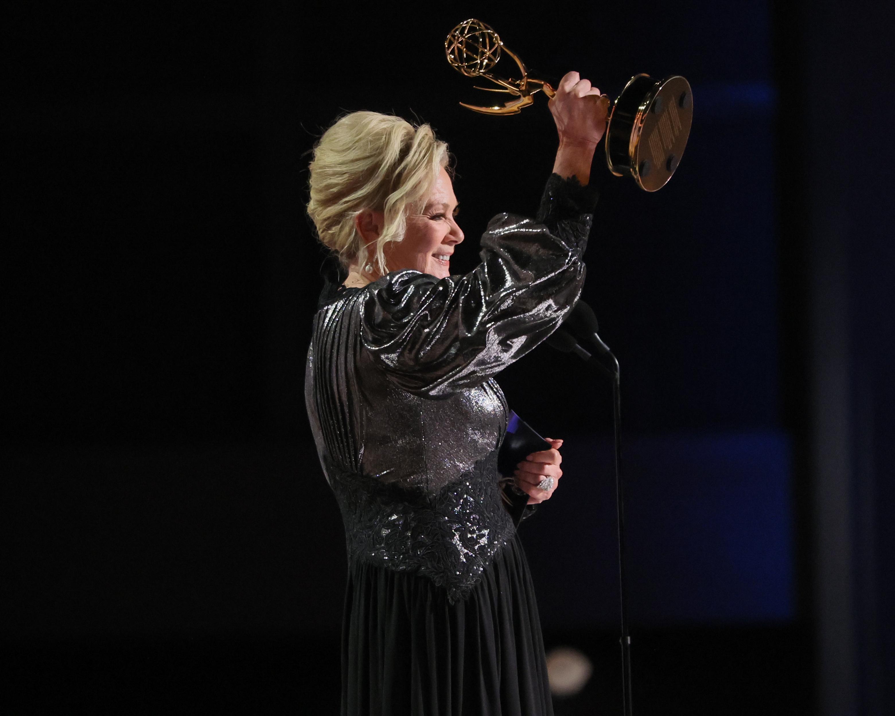 A woman in a black gown raises an Emmy statuette onstage.