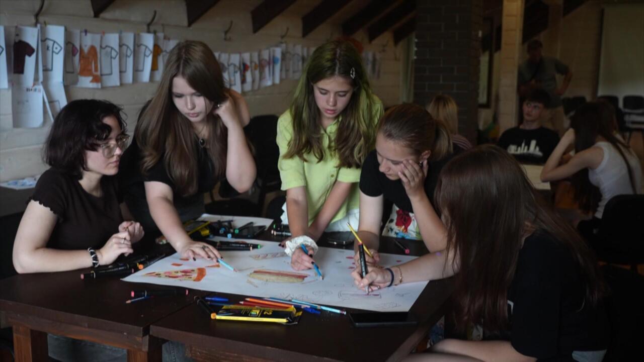 Teenagers gather around a table, drawing together with colored markers in a workshop.