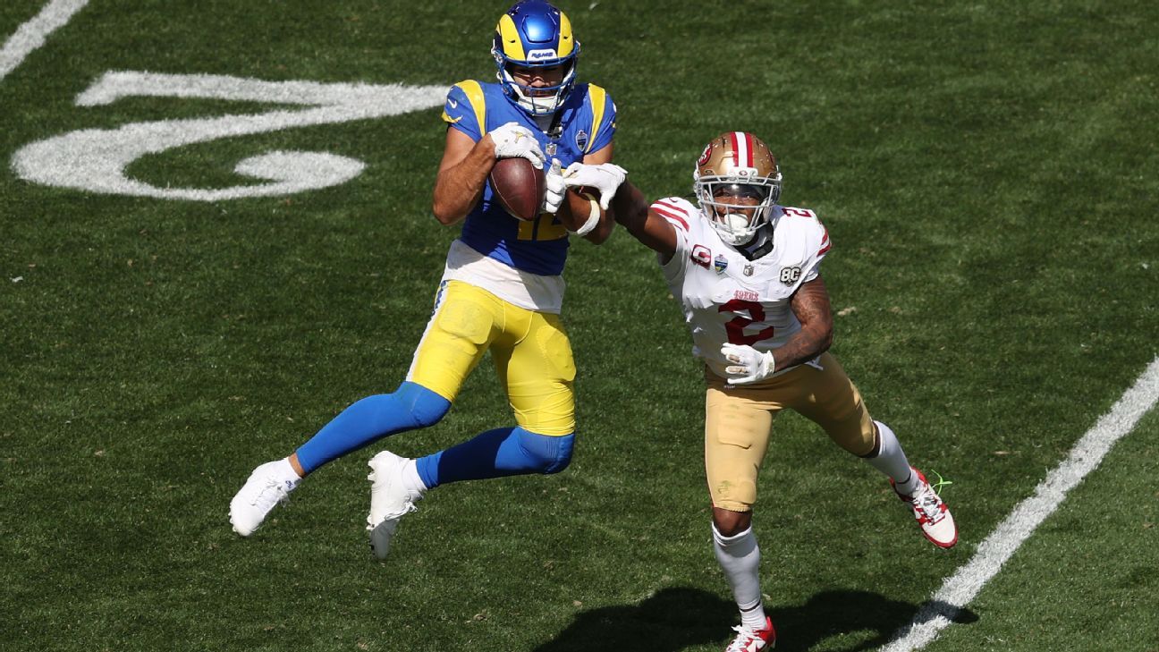 A Rams player carries the football as a 49ers defender reaches toward him on the field.
