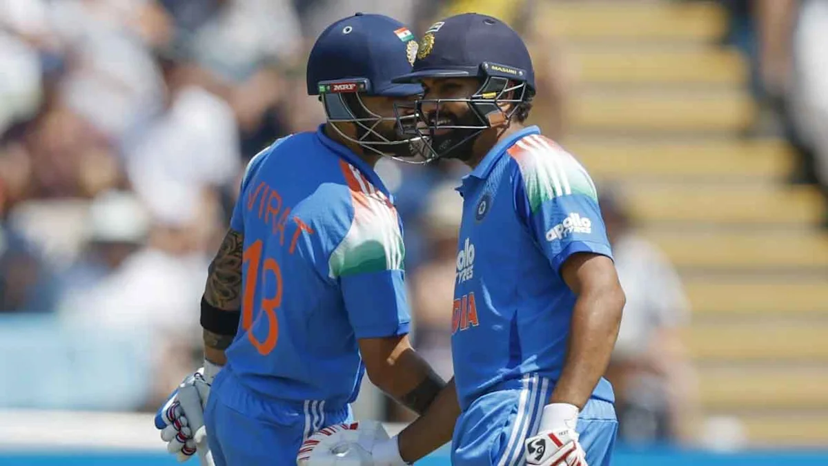 Two Indian cricket players in blue uniforms and helmets stand together on the field.
