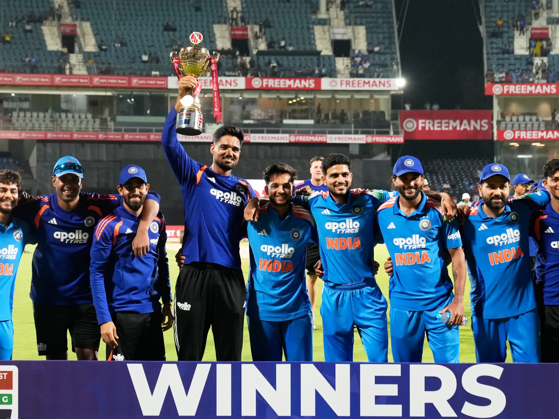 Indian cricket players pose together, one lifting a trophy, after winning a match
