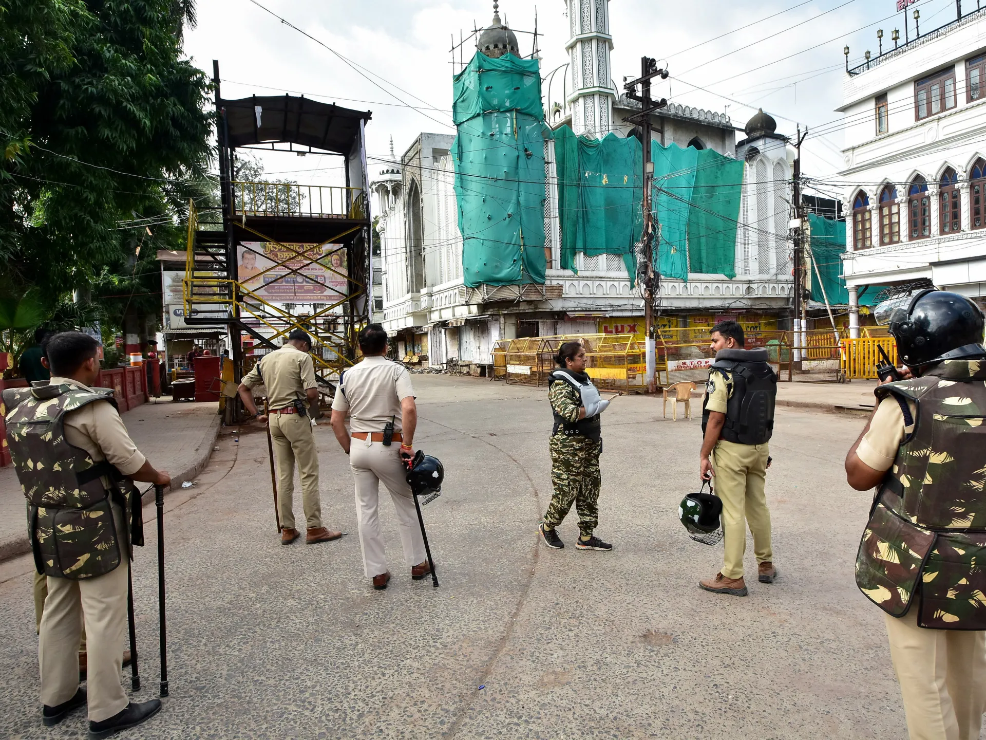 Police stand on a cordoned street outside a mosque partly covered with green construction netting.