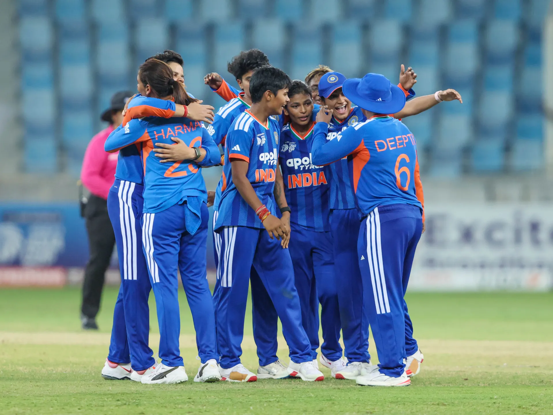Indian women cricketers in blue uniforms celebrate together on the field