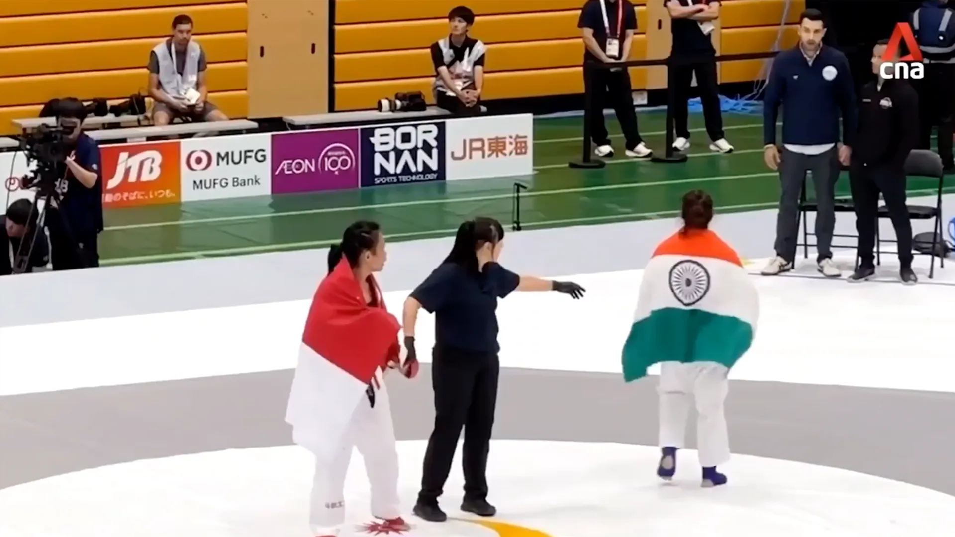 Athlete draped in India’s flag walks away as an official extends an arm nearby.