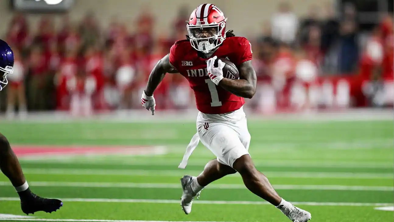 Indiana player in a red jersey runs with the football during a game.