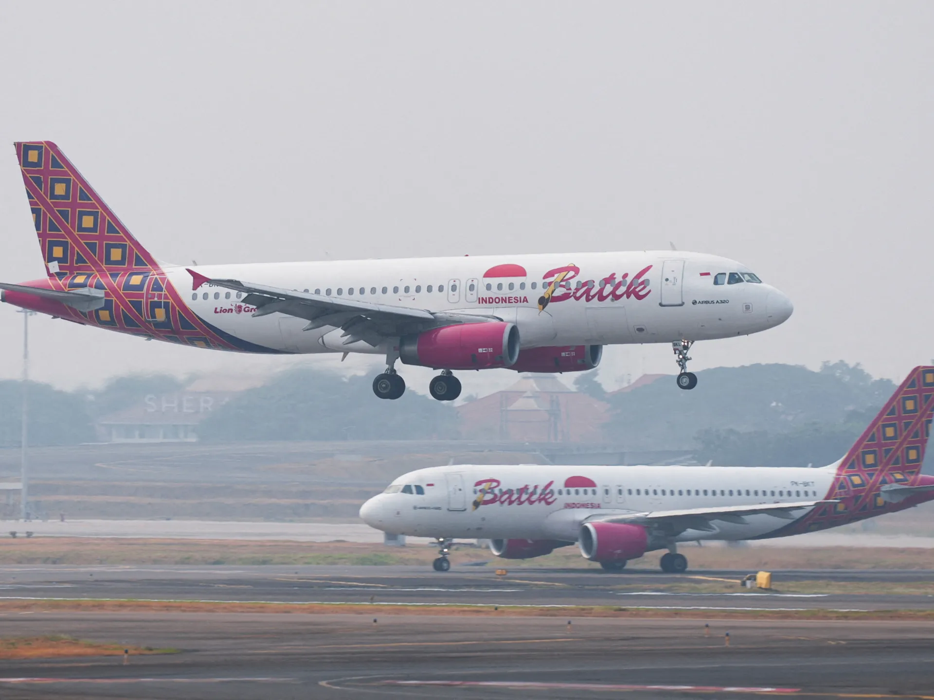 Two Batik Air passenger jets at an airport, one landing and another taxiing on the runway