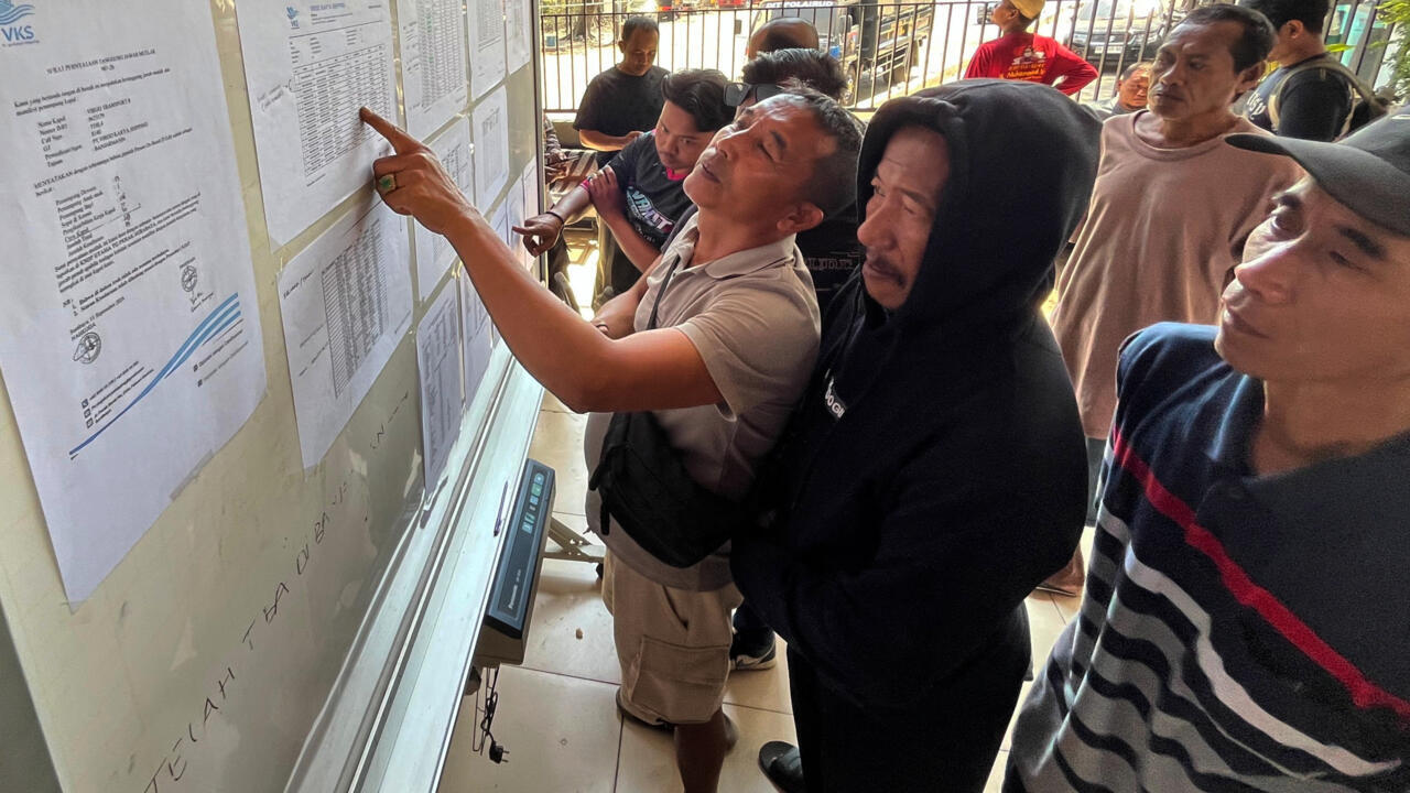 People examine posted documents as one man points to a list.