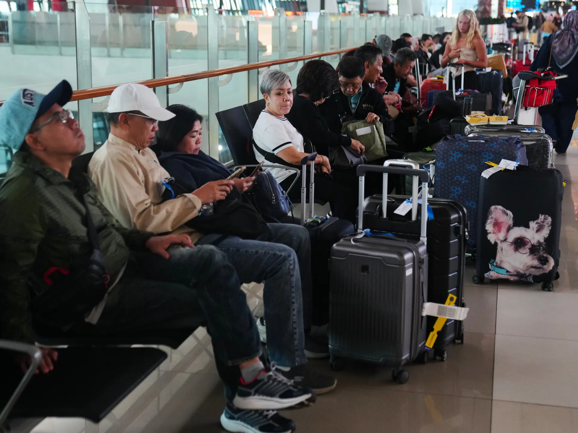 Passengers wait with luggage in an airport terminal seating area.
