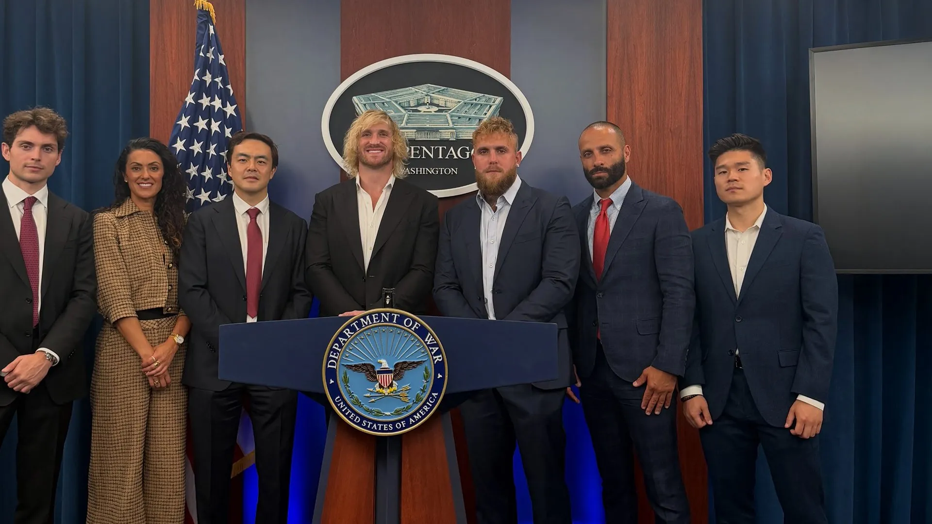 Seven people pose beside a Pentagon podium beneath U.S. and Defense Department emblems.