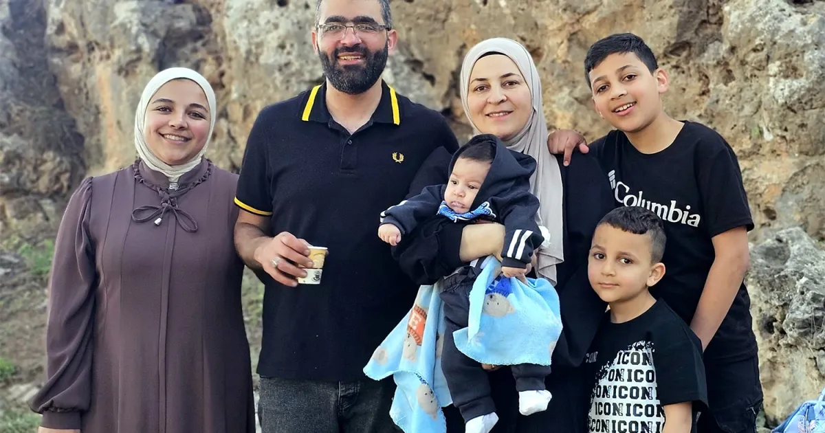 Six adults and children, including a baby, pose together before a rocky outdoor backdrop.