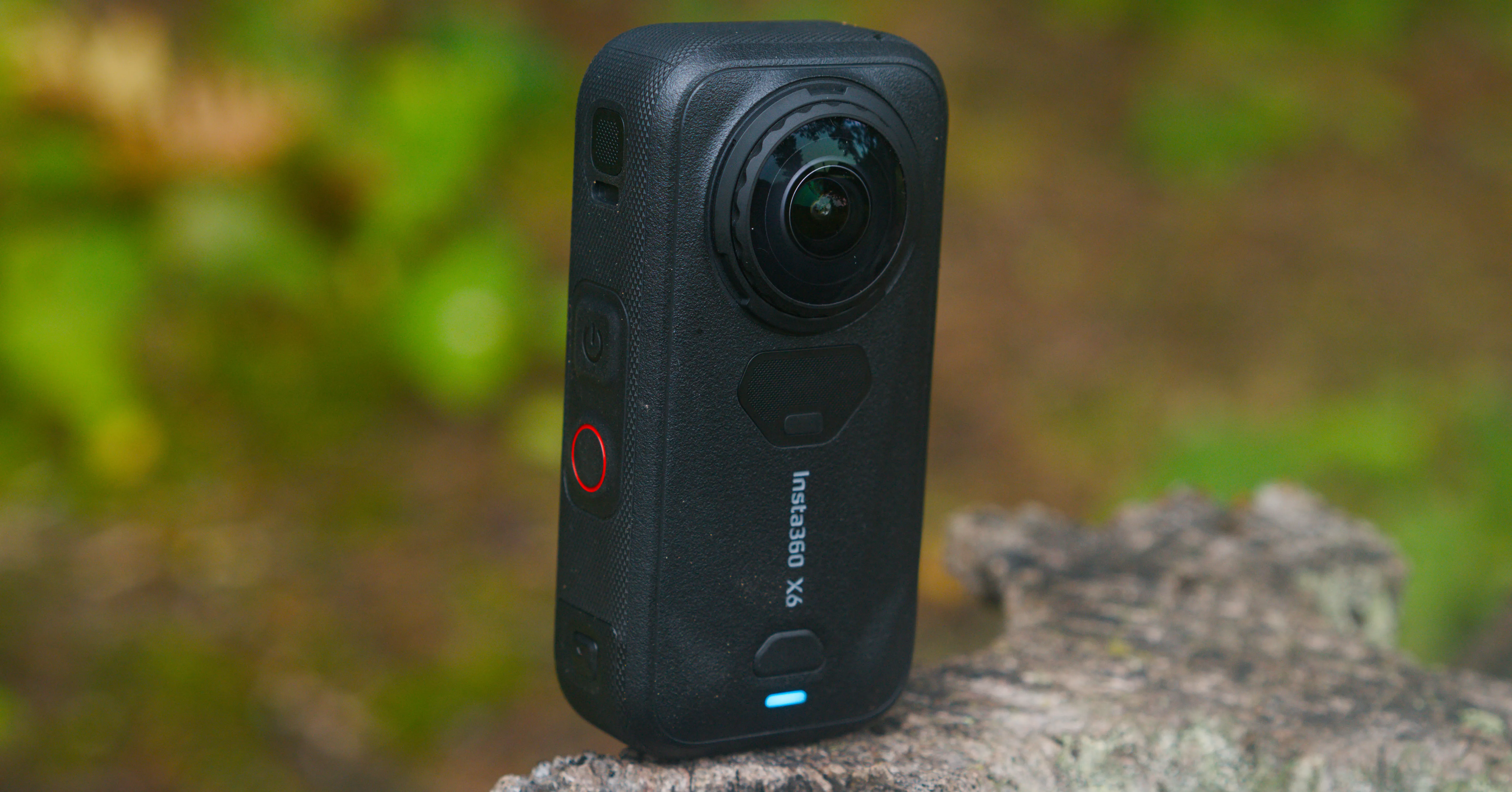 Insta360 X6 camera standing upright on a rock against a blurred green outdoor background