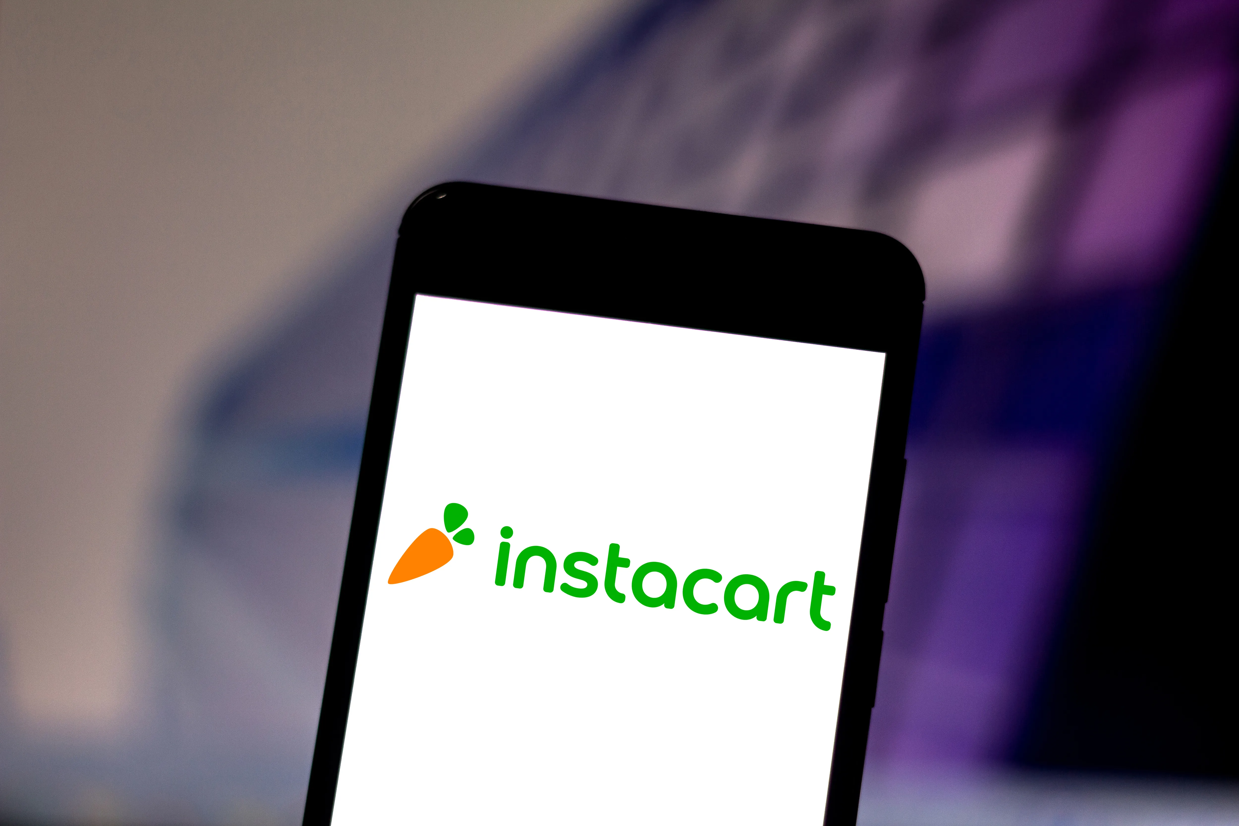 Smartphone displaying the Instacart logo against a dark, purple-lit background.