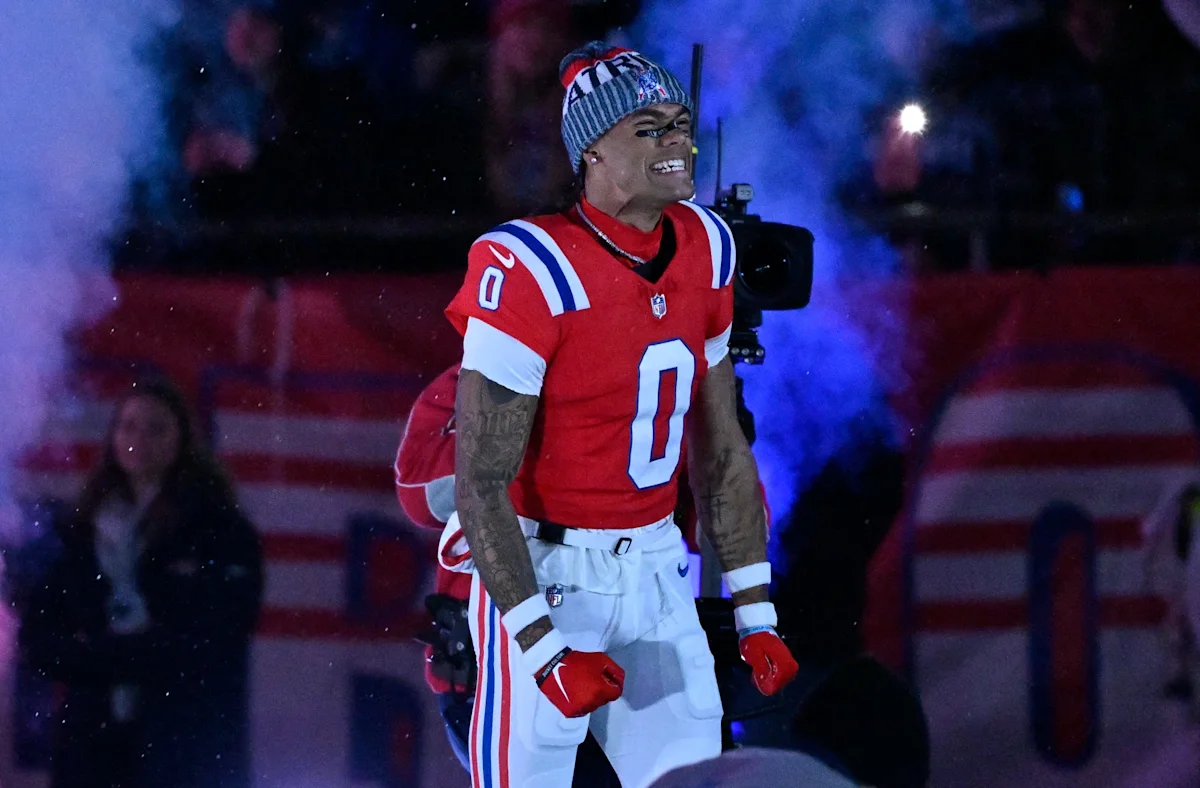 Patriots football player in red jersey and knit hat stands amid blue smoke during a game