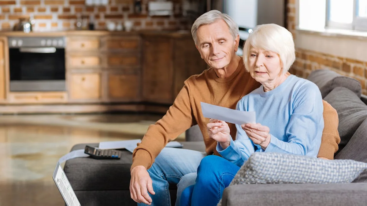 Older couple reviews a letter together while seated on a living room sofa.