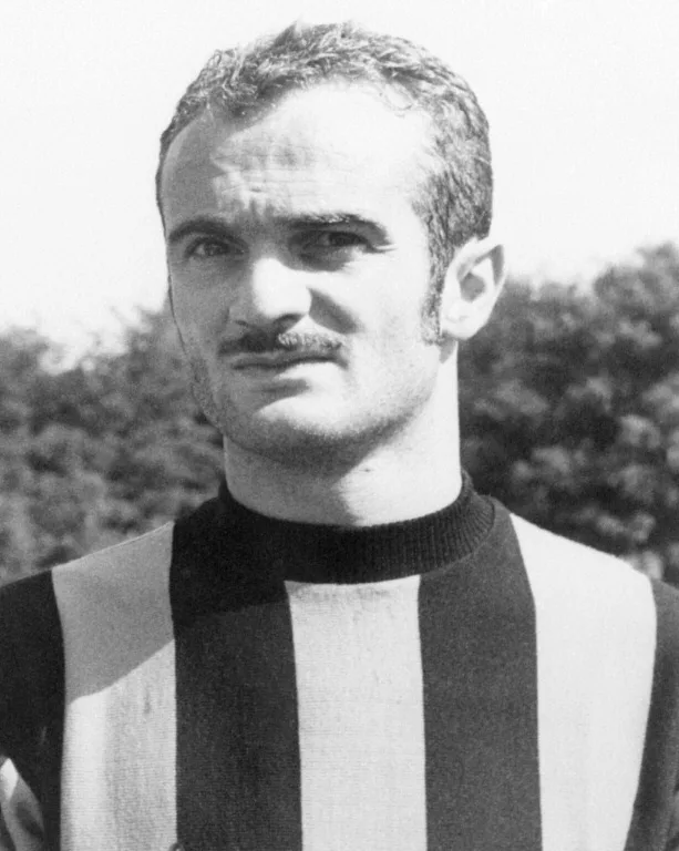 Black-and-white portrait of a mustached footballer wearing a vertically striped jersey