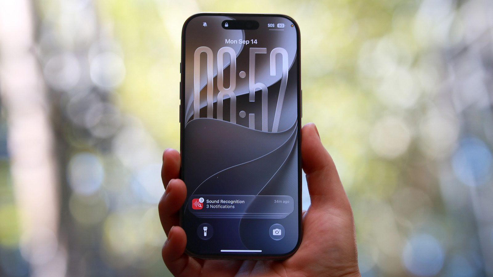 Hand holding a smartphone displaying a lock screen against a softly blurred outdoor background