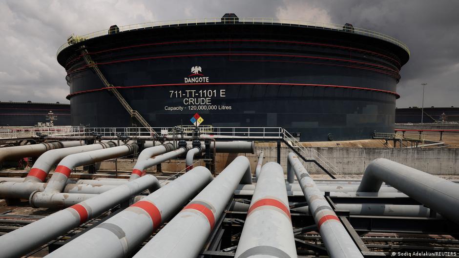 Large crude oil storage tank surrounded by interconnected industrial pipelines under dark storm clouds