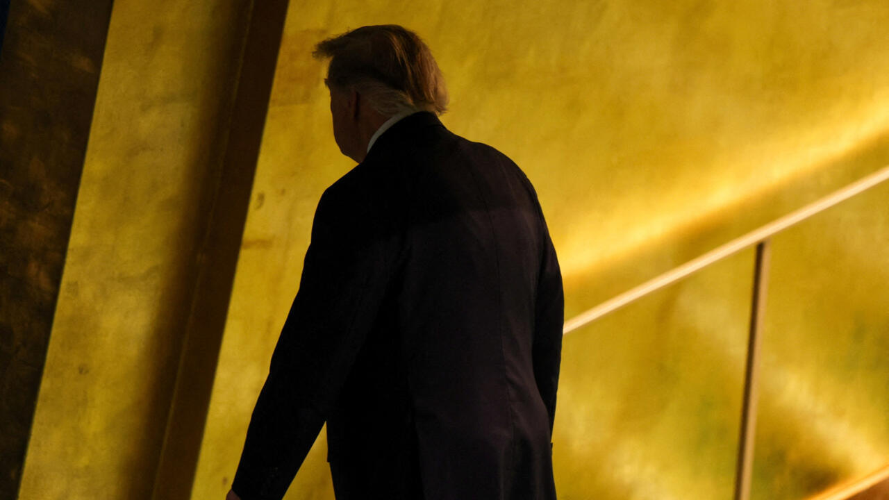 A man in a dark suit walks up a staircase through a warmly lit interior.