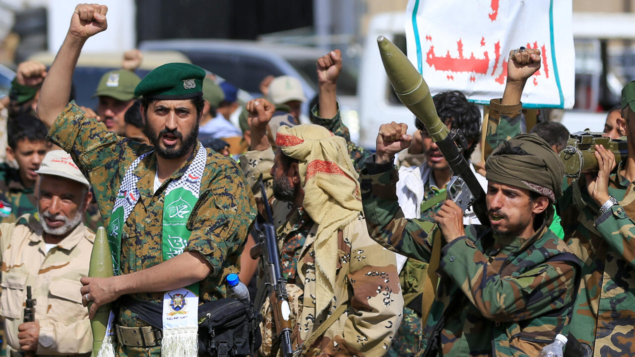 Armed men in military-style clothing raise fists during a crowded public gathering.