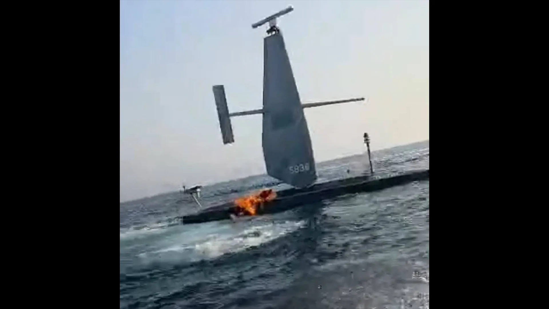 Uncrewed sail-equipped vessel burns on rough sea, with a tall mast and crossbars visible.