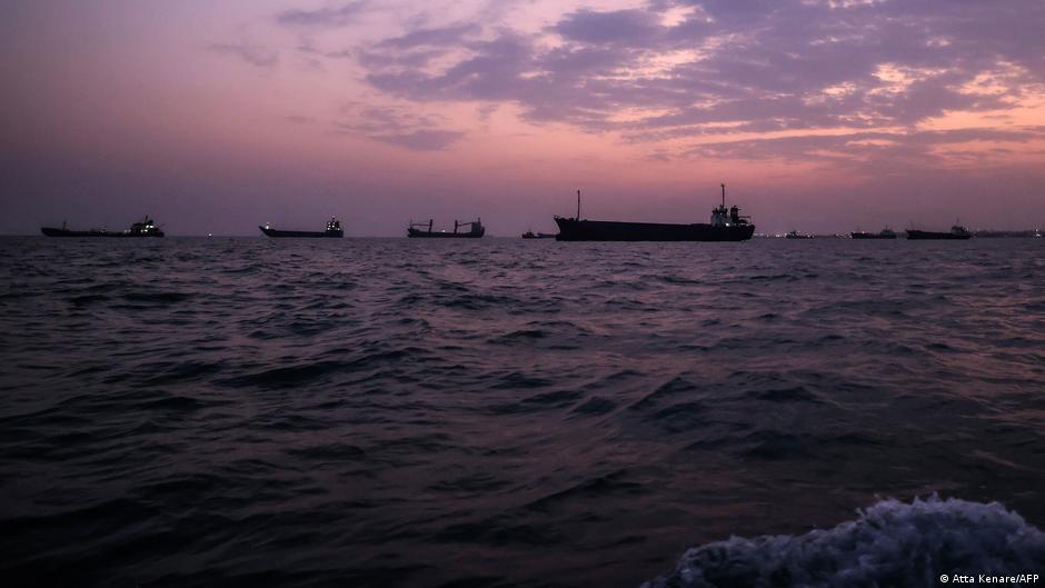 Cargo ships silhouetted on dark water beneath a pink and purple dusk sky