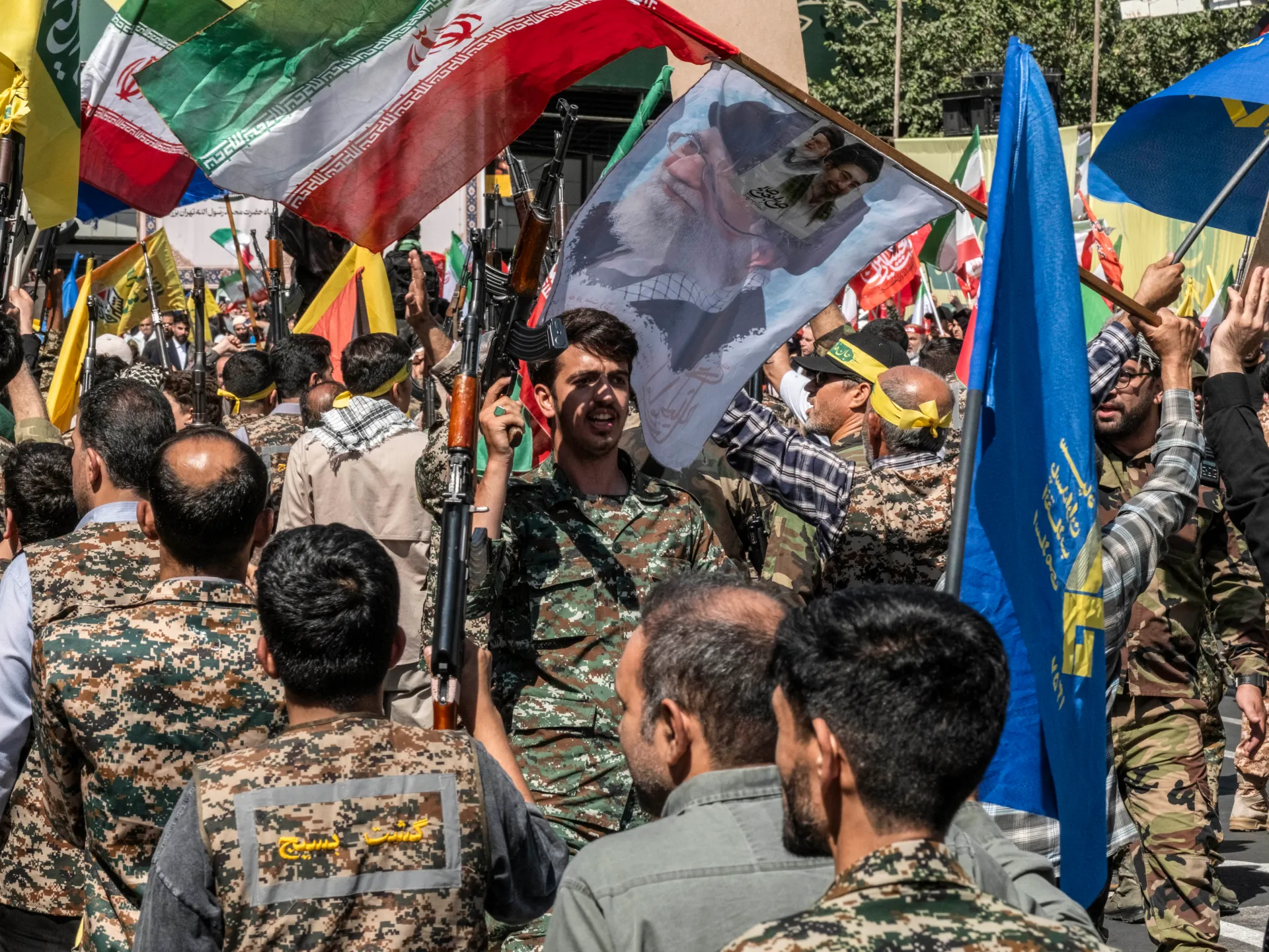 Crowd of armed men holding Iranian flags and portraits during a public gathering