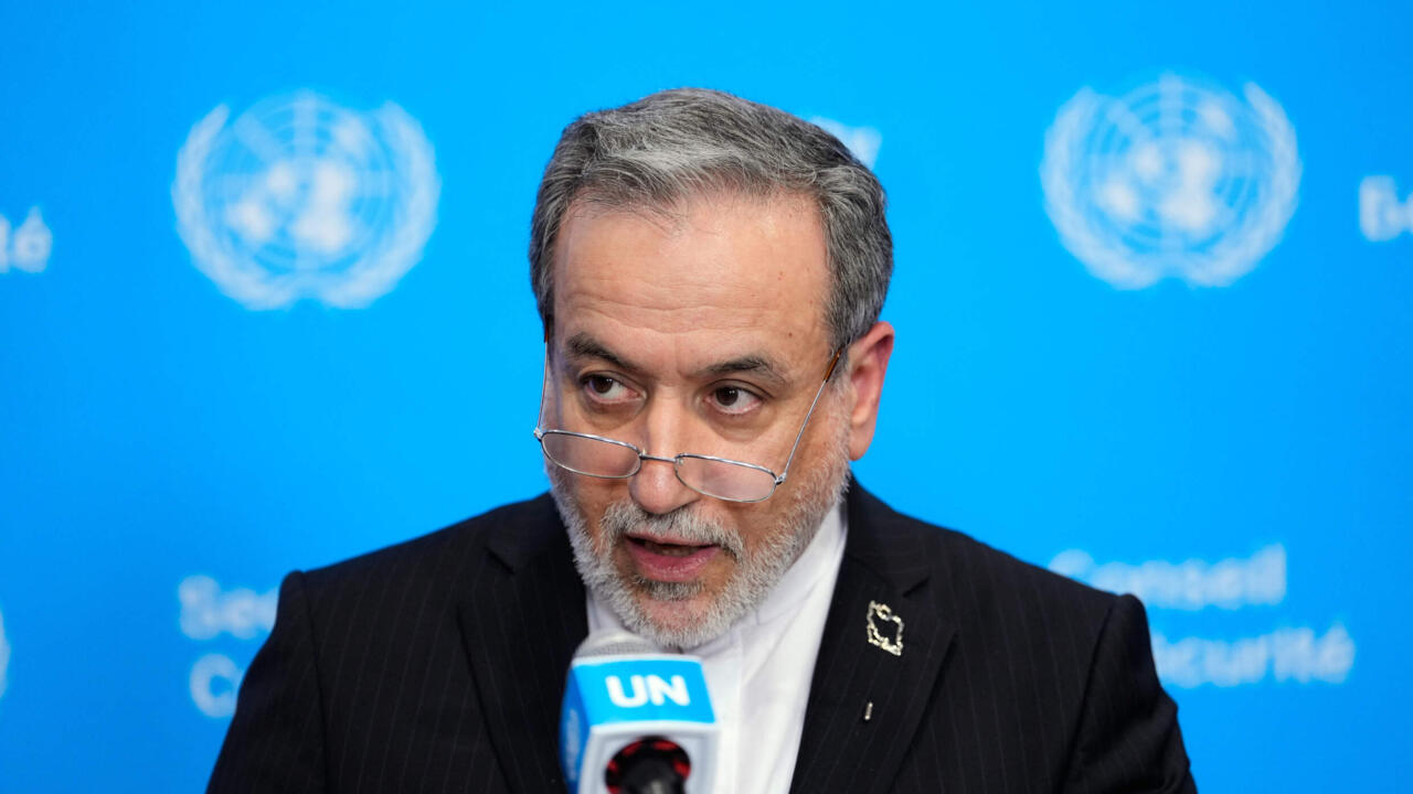 Gray-haired man in a dark suit speaks into a UN-branded microphone against a blue backdrop.