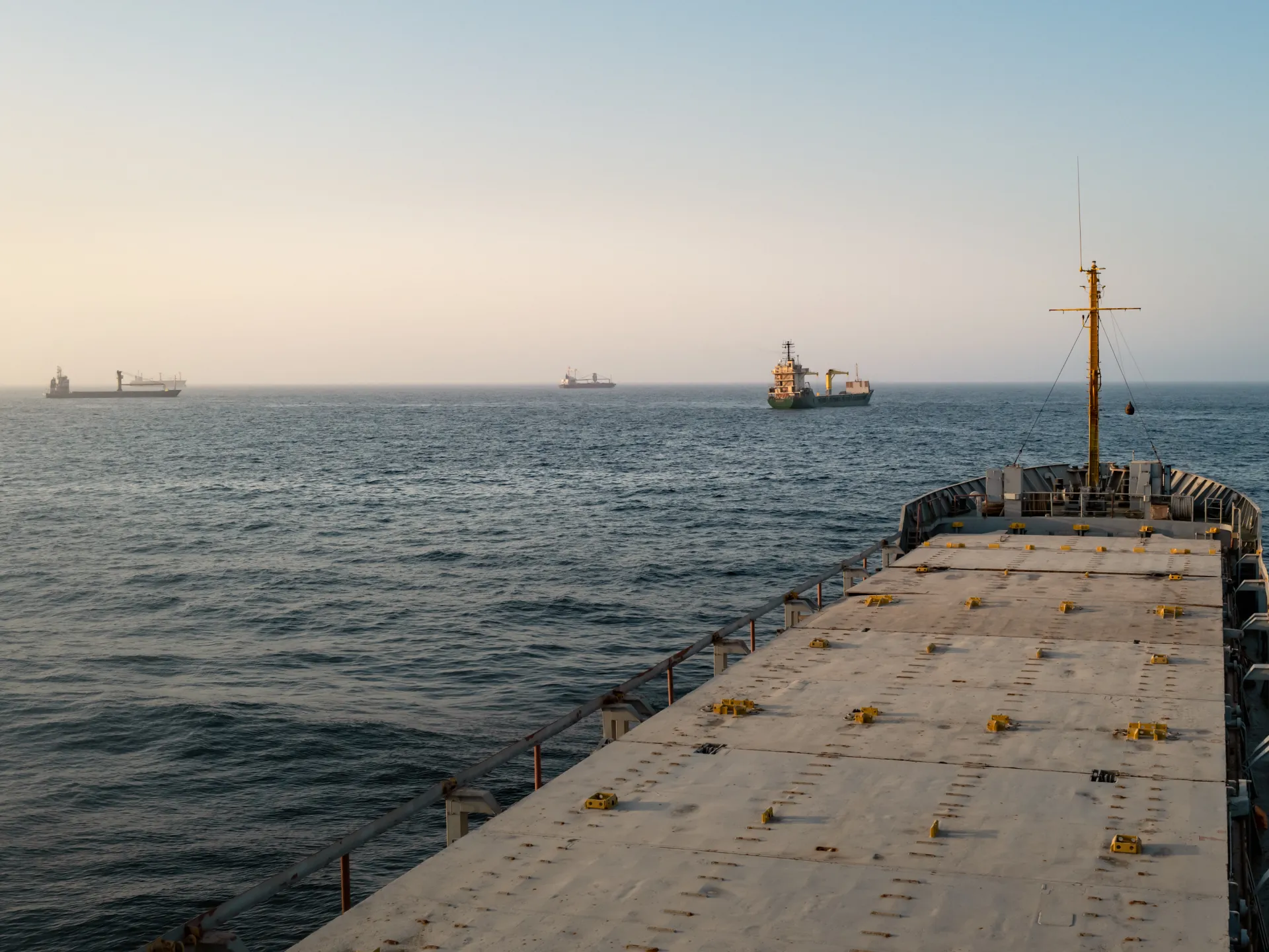Cargo ship deck facing open sea with several vessels visible on the hazy horizon